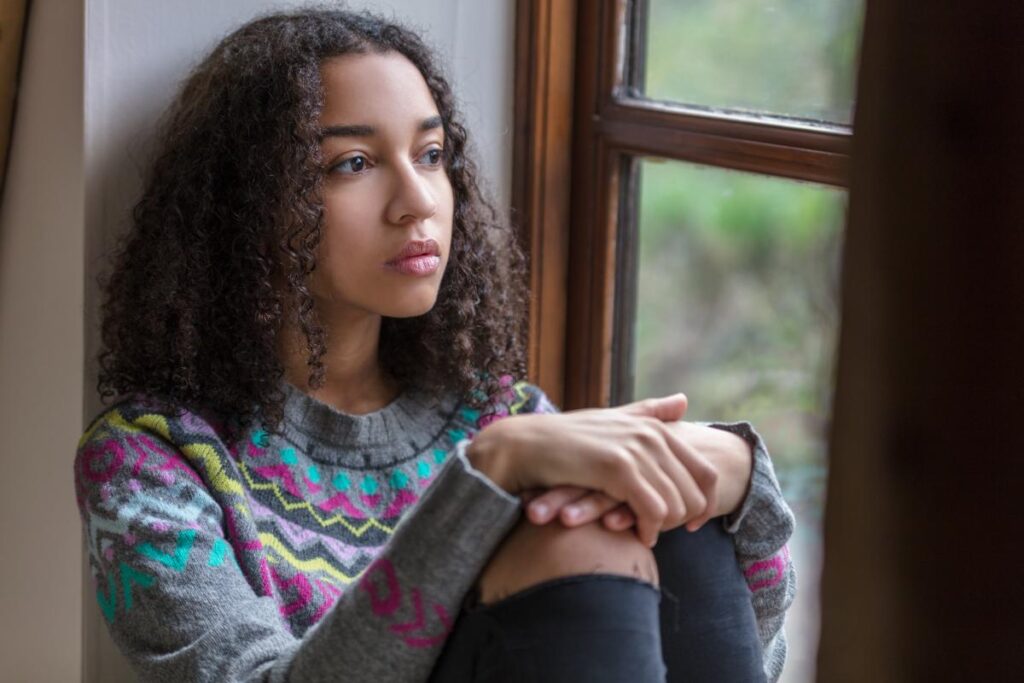 a teen genetically susceptible to depression sits against a wall