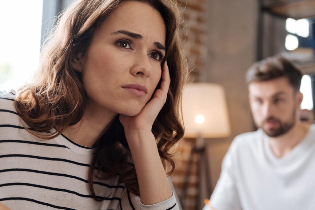 a woman looks sadly away from the camera wondering how to deal with a spouse who relapses while her husband looks sadly away