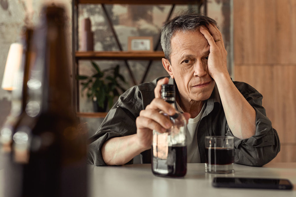 A man stares at a bottle, and wonders do i need to go to rehab for binge drinking