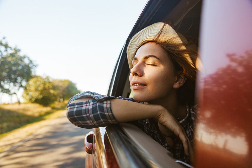 A young woman leans out the car window and relaxes after reading SOBER: A 5 Point Survival Guide to Your First Year Post-Rehab
