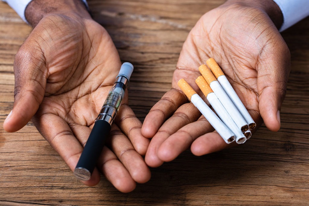 A man holds an e-cigarette and cigarettes, and thinks about how tobacco use is a major health concern