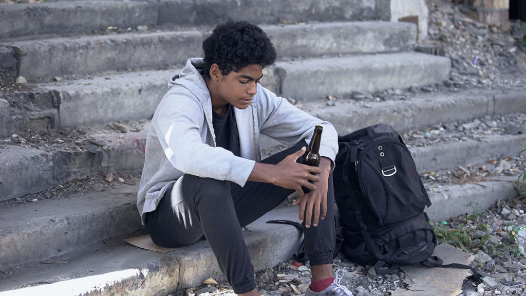 A teen sits on the steps with a bottle of beer and wonders why do teenagers drink alone