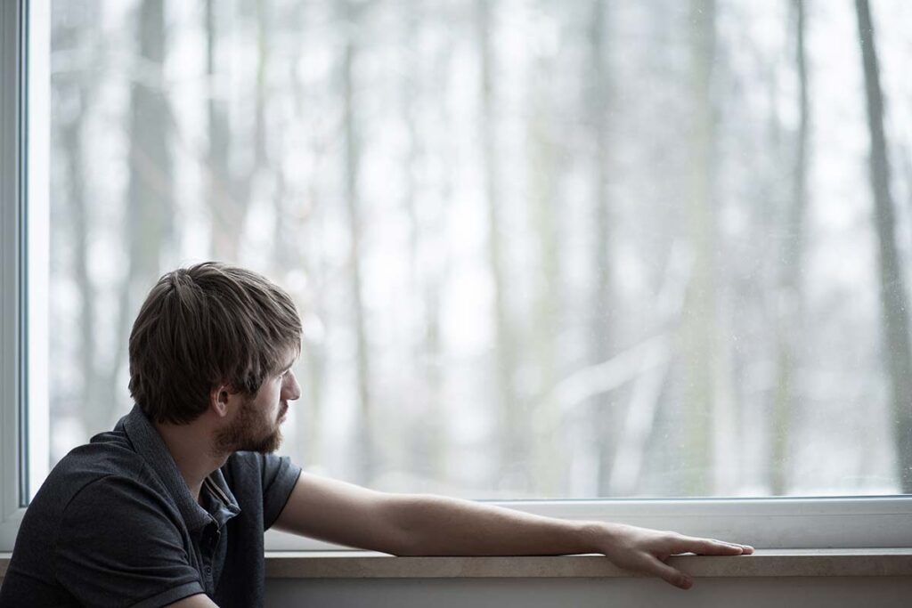 a man stares out a window thinking about the common reasons he began abusing drugs