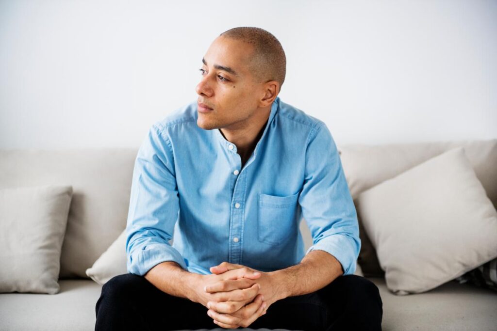 young man sitting on his couch wondering are binge drinkers and alcoholics the same