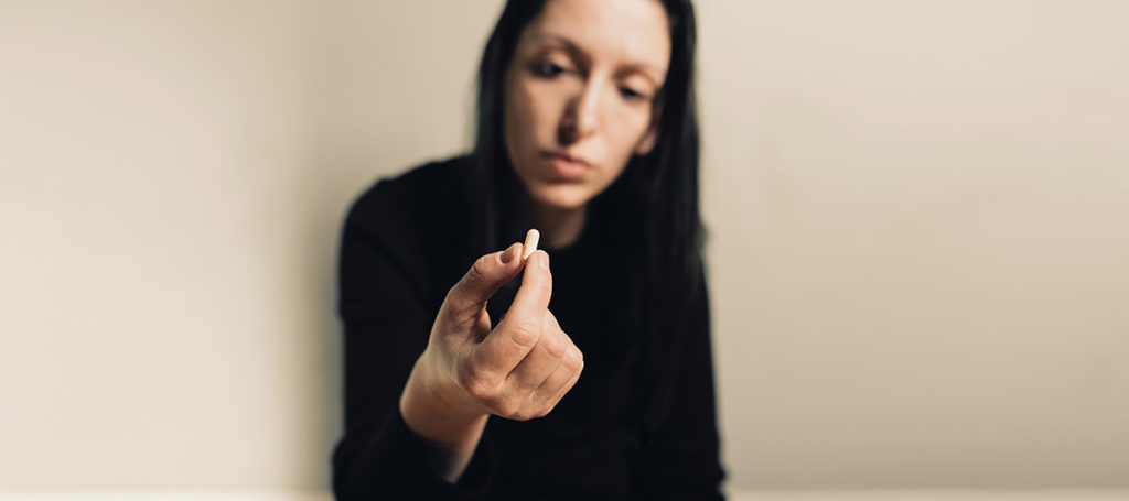 woman holding prescription pill between fingers thinking about the difference between opioids and opiates