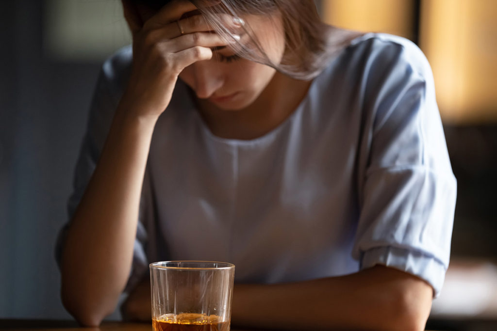 woman holding head with alcoholic drink on table showing emotional effects of alcohol on mood