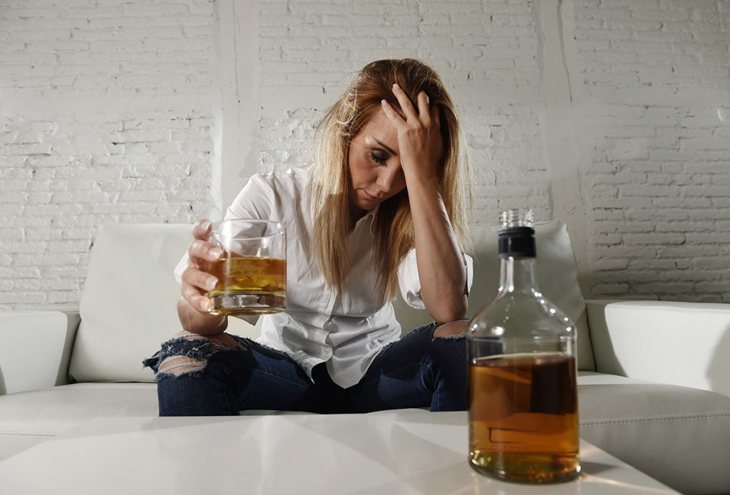 woman putting down glass of scotch suffering physical effects of alcohol on the body