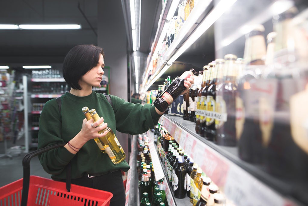 a woman in a store taking alcohol from a shelf wondering why is alcohol addictive