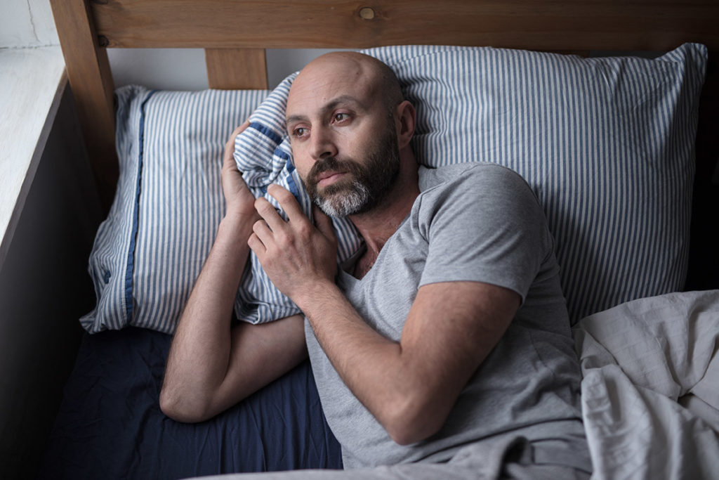 a man lies in bed thinking about the dangers of substance abuse