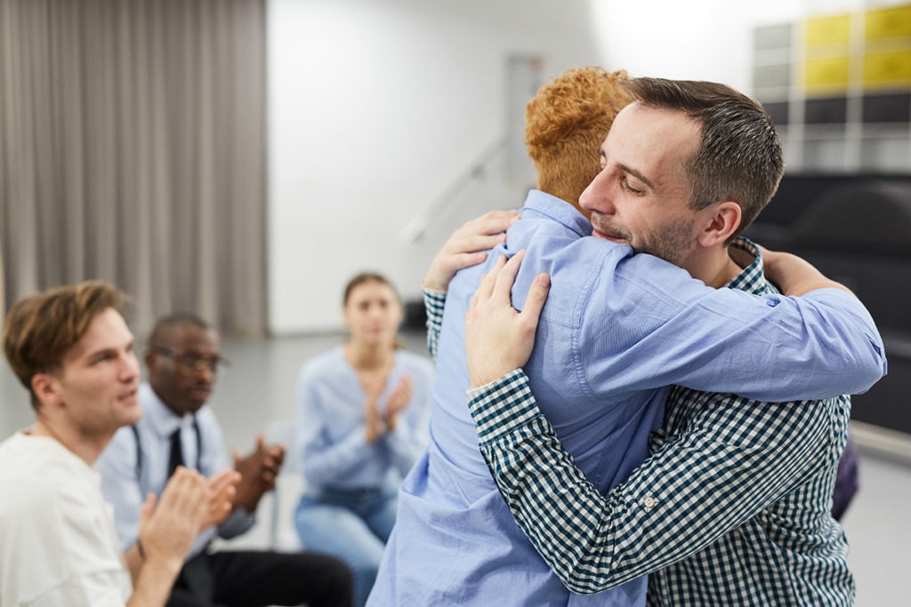 a man hugs another man as they discuss the heroin addiction recovery rate