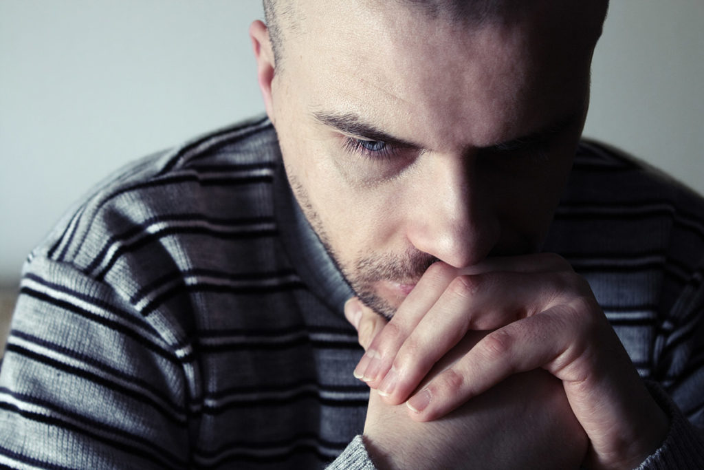 a man rests his chin on his hands as he thinks about telltale addictive behaviors