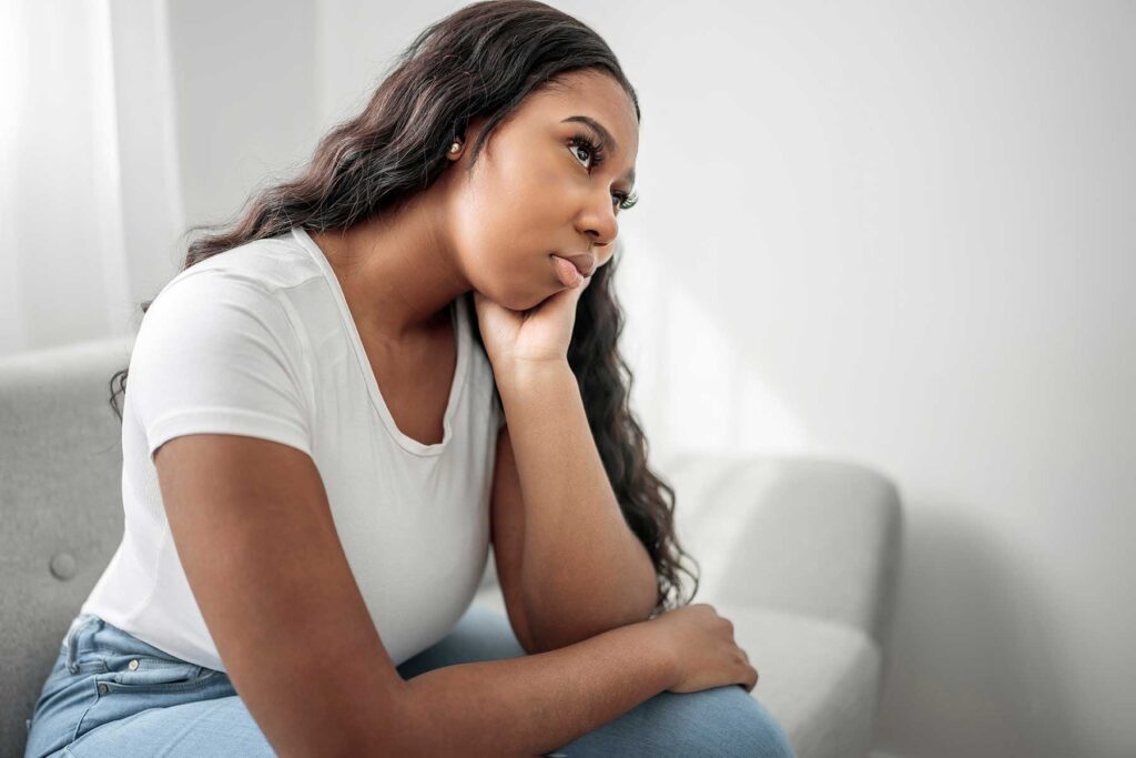 a teen sits on a couch with their head in their hand and looks sad and shows signs of depression for a teenager