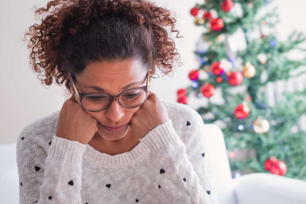 Woman looking defeated near Christmas tree, hoping to survive the holidays despite addiction