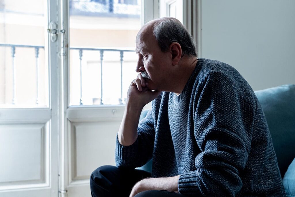 a senior with Late-Onset Alcoholism sits on a bed pondering life