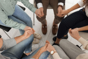 a group of people hold hands while sitting in chairs in a circle in a painkiller rehab program