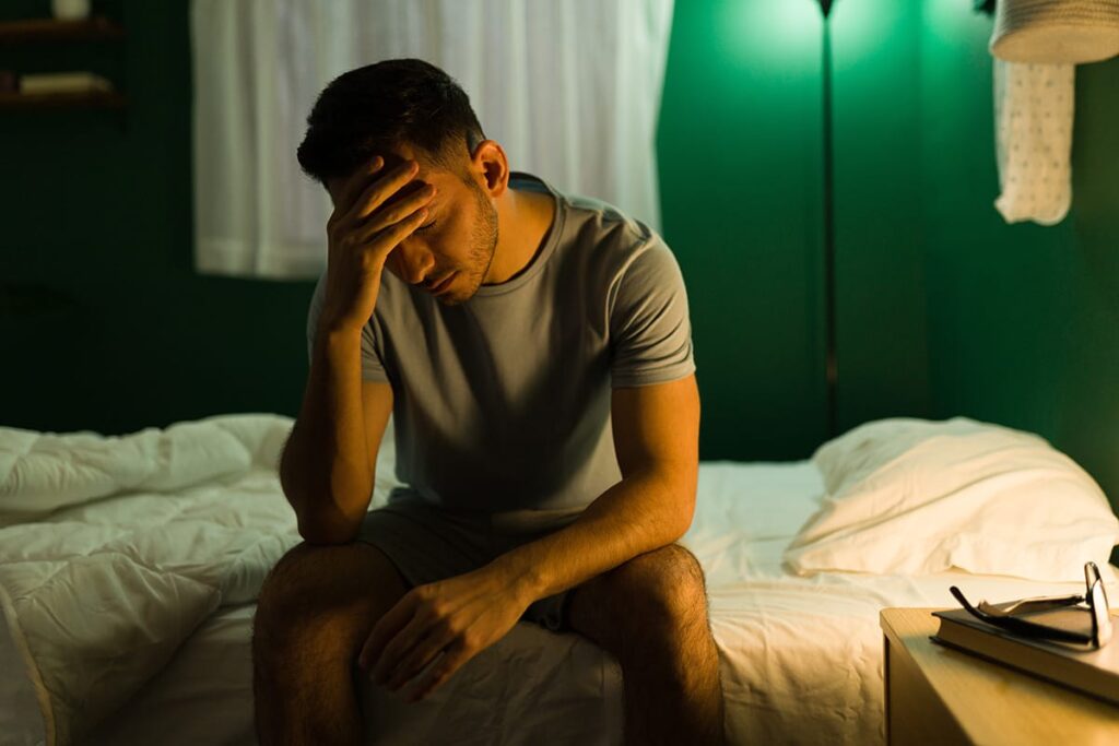 Man sits on bed holding head with shame after yet another brown out