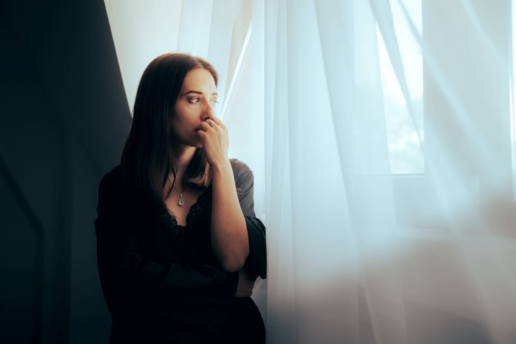 Woman leans by curtains and thinks about derealization and addiction