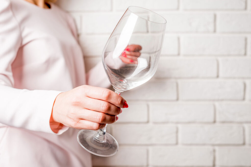 Hand of a person holding a wine glass, wondering how drinking alone and alcoholism are linked