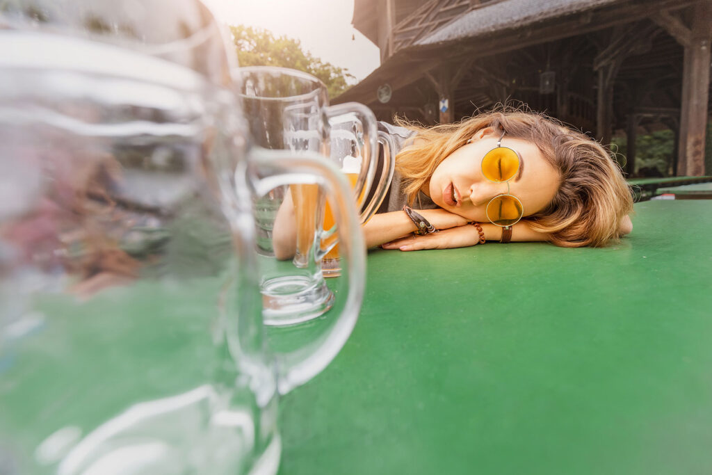 Woman passed out at table while her friends talk about how to tell if someone is abusing alcohol