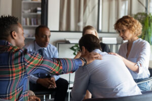 People comfort a man in group therapy at a heroin addiction treatment center